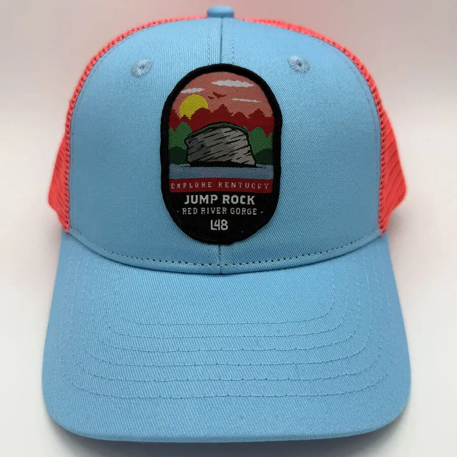 Blue trucker hat with red mesh, patch showing a sunset over mountains and a rock formation, text reads 'Explore Kentucky Jump Rock Red River Gorge'.