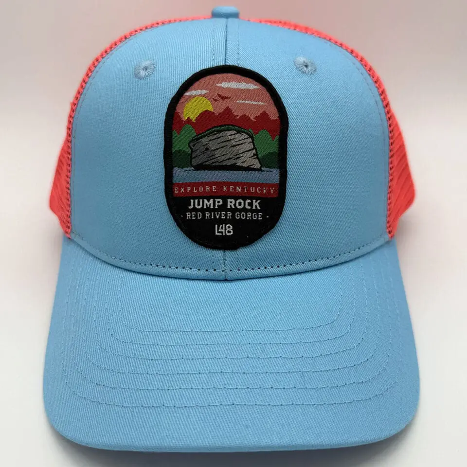 Blue Trucker Hat with Red Mesh, Patch Showing a Sunset over Mountains and a Rock Formation, Text Reads 'explore Kentucky Jump Rock Red River Gorge'.